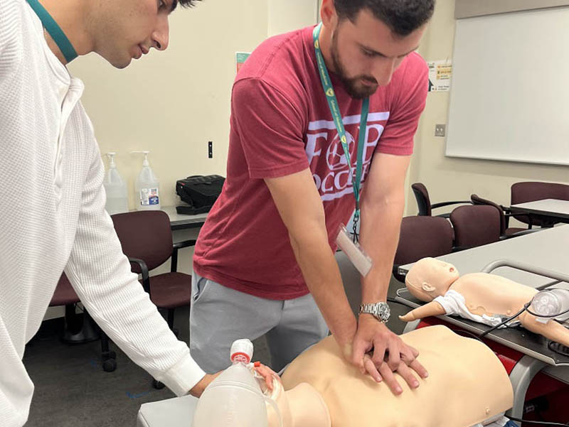 Two students practice CPR on a dummy