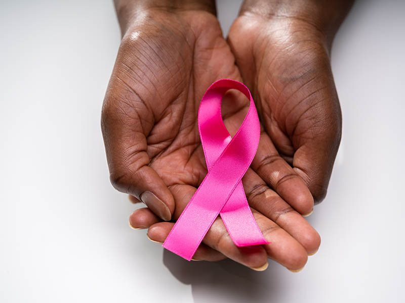 A pair of hands hold a pink Breast Cancer Awareness Month ribbon 