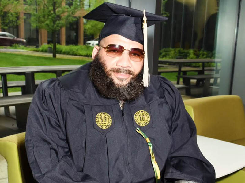 Yannick Washington sits wearing his graduation cap and gown